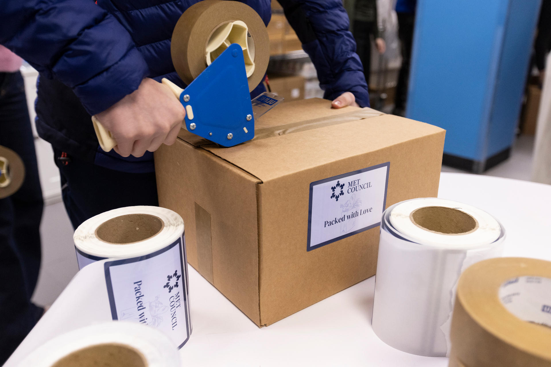Met Council volunteer sealing a 'Packed with Love' food box for delivery